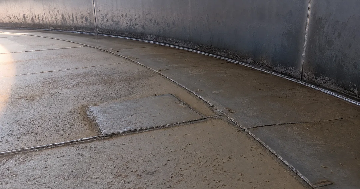 Clean storage-tank floor showing annular plates, lap welds, a repair patch, and localized pitting